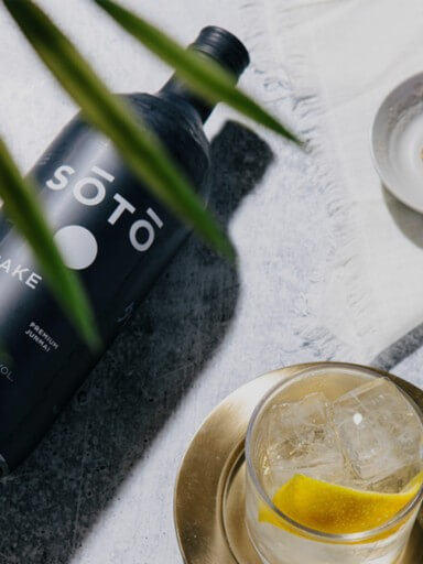 Garrafa de Sake Soto deitada no cimento com coktail ao lado, exclusivo da garrafeira Black Pepper and Basil