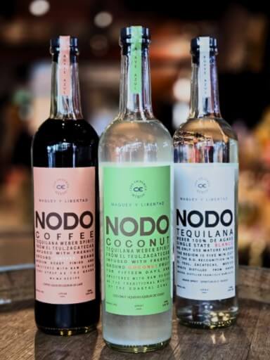 Three bottles of Nodo agave distillate on a bar counter