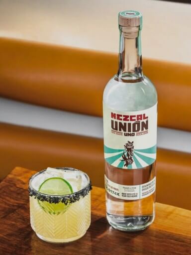Bottle of Mezcal Únion on the table with a cocktail next to it.