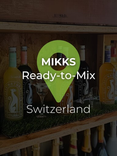 Several Mikks Drinks bottles with two margarita glasses on a cork shelf from the Black Pepper and Basil wine rack, with an artificial grass mat underneath_1